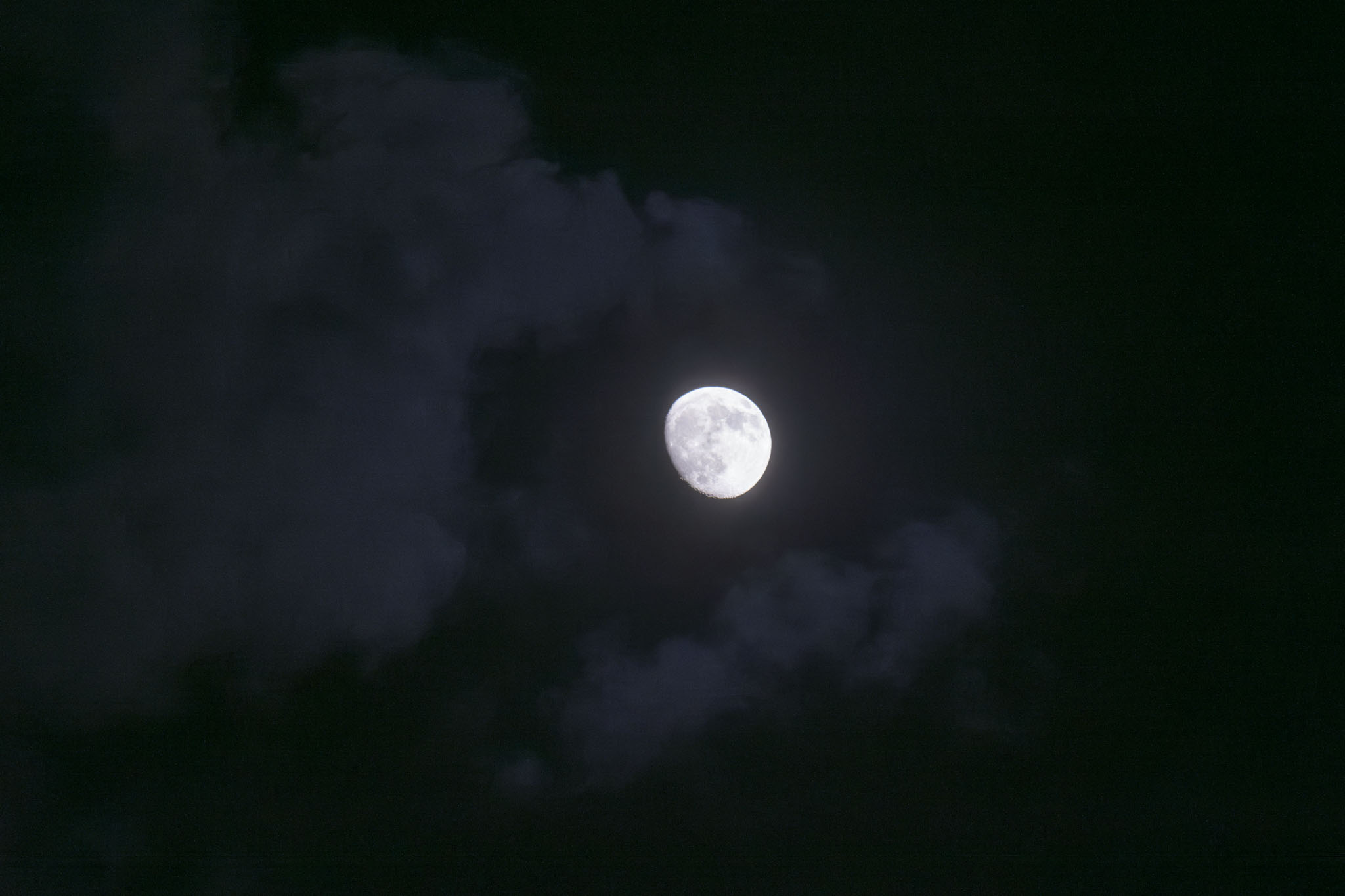 The moon shines in a dark sky lighting clouds around it